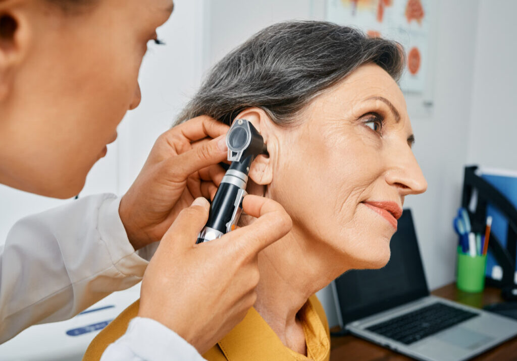 Hearing test for mature people, otoscopy. Otolaryngologist doctor checking senior woman's ear using otoscope or auriscope at medical center